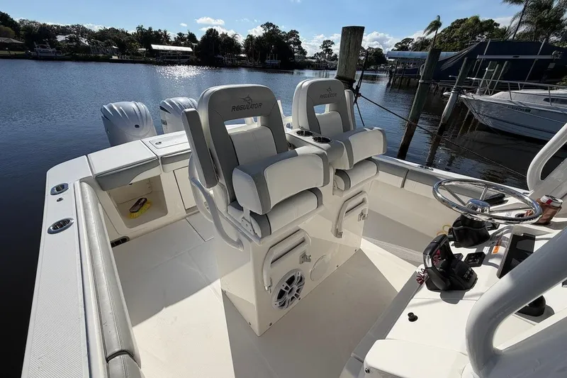 Slide: The Image of 2022 Regulator 28 boat interior with dual seats and steering wheel, docked by a serene lake. - 11