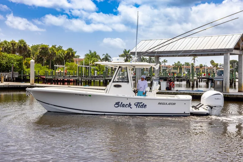 Slide: The Image of 2022 Regulator 28 boat named "Slack Tide" on water near marina, under blue sky. - 11