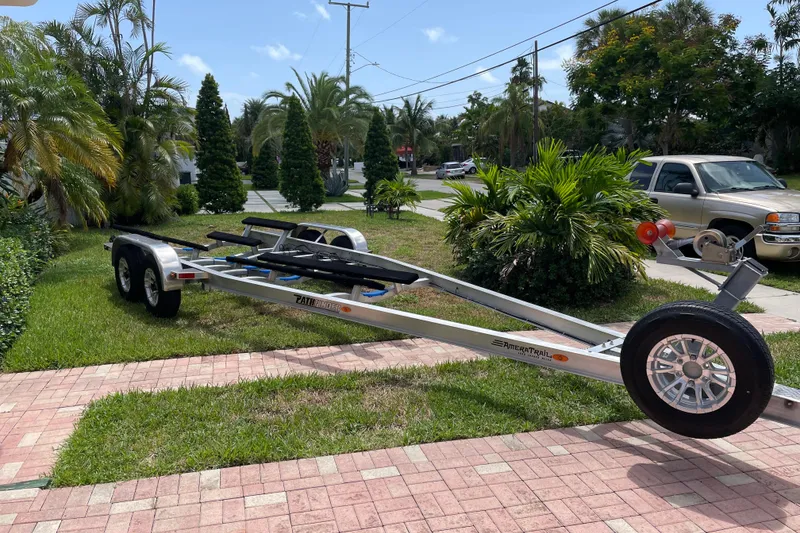 Slide: The Image of 2022 Pathfinder 2600 HPS boat trailer parked on a grassy driveway with palm trees. - 45