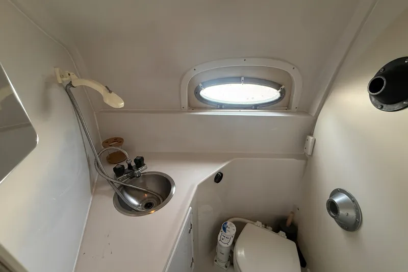 Slide: The Image of 1998 Four Winns 258 Vista boat bathroom with sink, toilet, and porthole window. - 23