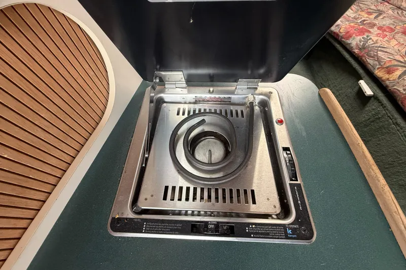Slide: The Image of 1998 Four Winns 258 Vista boat stove with single burner, open lid, and surrounding cabin details. - 30