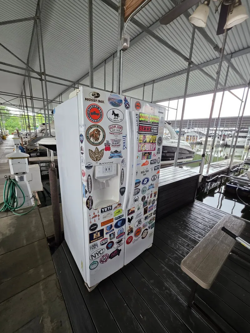 Slide: The Image of Sticker-covered fridge on dock beside Bennington 25LSB boat. - 44