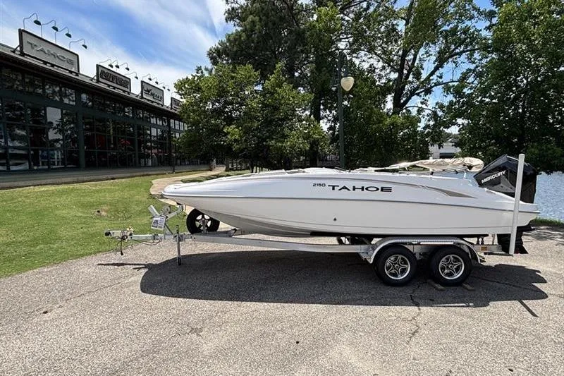 The Image of 2026 Tahoe 2150 boat on trailer, parked near dealership, surrounded by trees and water. - 0