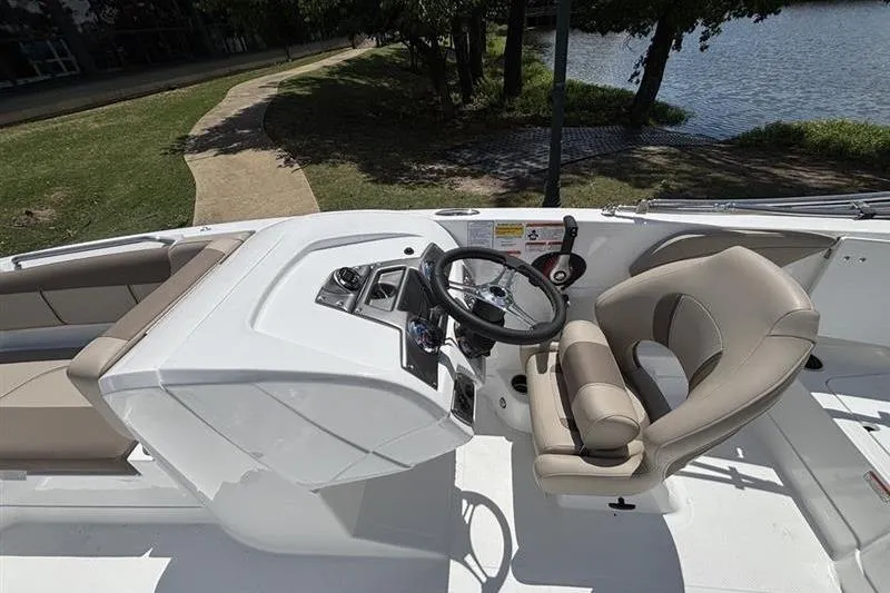 Slide: The Image of 2026 Tahoe 2150 boat cockpit with steering wheel and seating, near a lakeside path. - 12