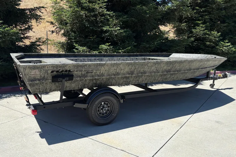 Slide: The Image of 2026 Tracker Grizzly 1860 Utility boat on trailer, parked outdoors, surrounded by trees. - 5