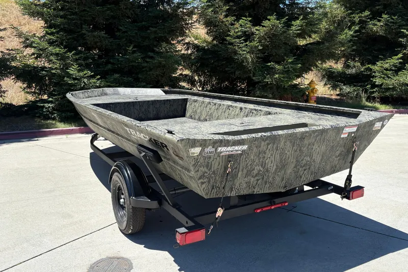 Slide: The Image of 2026 Tracker Grizzly 1860 Utility boat on trailer, parked outdoors, surrounded by trees. - 15