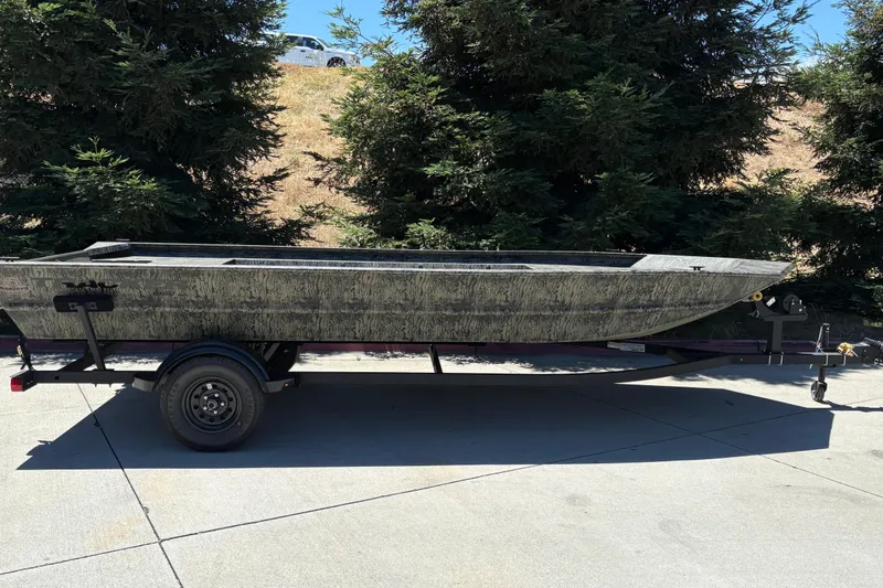 The Image of 2026 Tracker Grizzly 1860 Utility boat on trailer, parked outdoors near trees. - 0