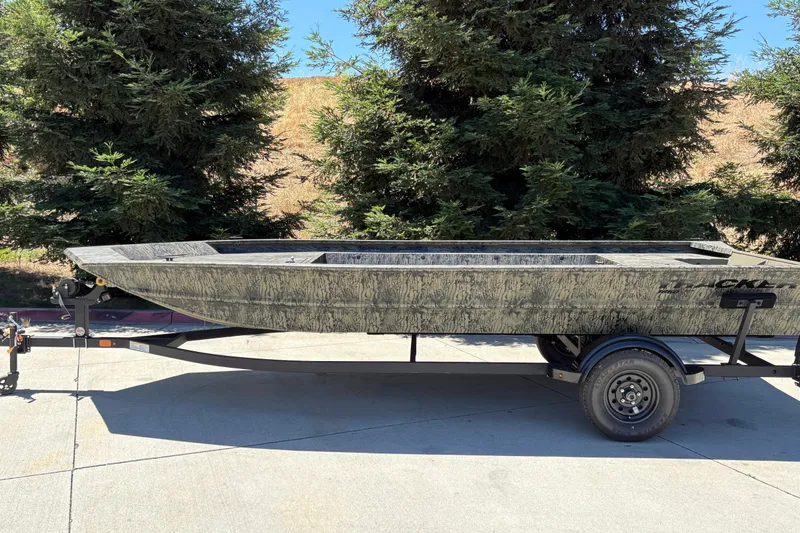Slide: The Image of 2026 Tracker Grizzly 1860 Utility boat on trailer, parked outdoors near trees. - 2