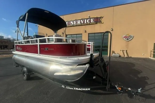 The Image of 2026 Sun Tracker Bass Buggy 16 XL Select pontoon boat on trailer outside service center. - 0