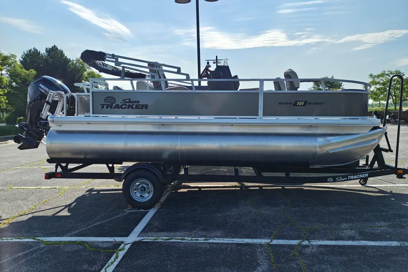 The Image of 2026 Sun Tracker Bass Buggy 18 DLX pontoon boat on trailer in parking lot. - 1