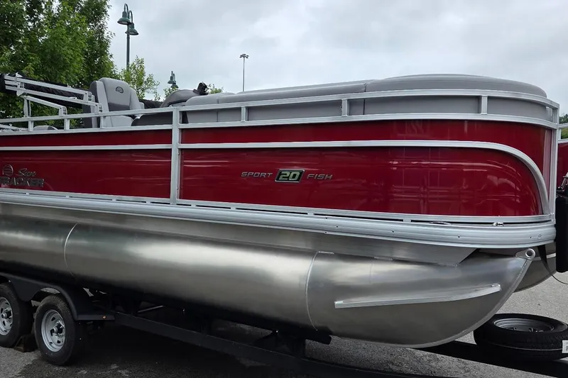 The Image of 2026 Sun Tracker SportFish 20 DLX pontoon boat with red and silver design on trailer. - 0