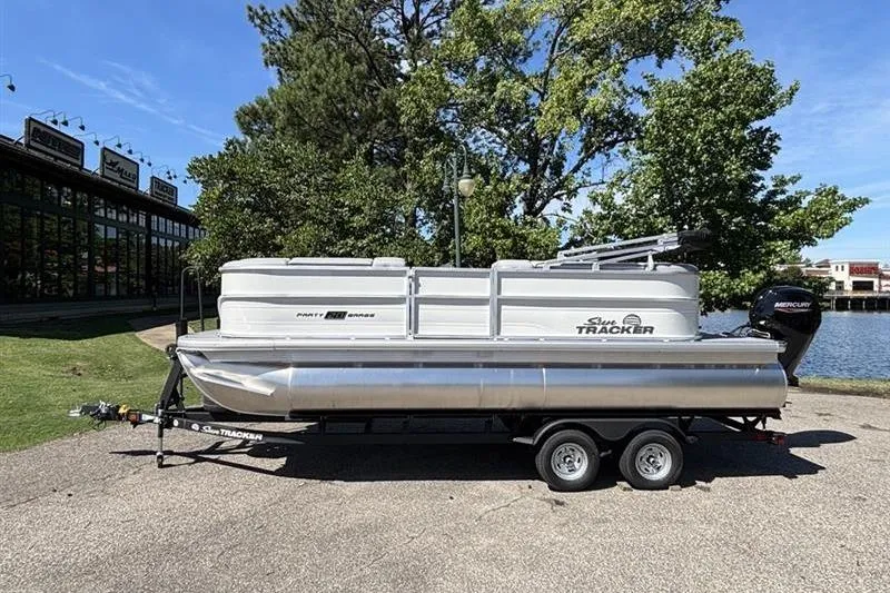 The Image of 2026 Sun Tracker Party Barge 20 DLX pontoon boat on trailer by a lake. - 0