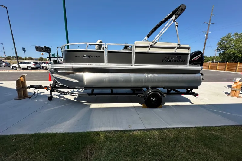 The Image of 2026 Sun Tracker Bass Buggy 16 XL Select pontoon boat on trailer, parked outdoors. - 0