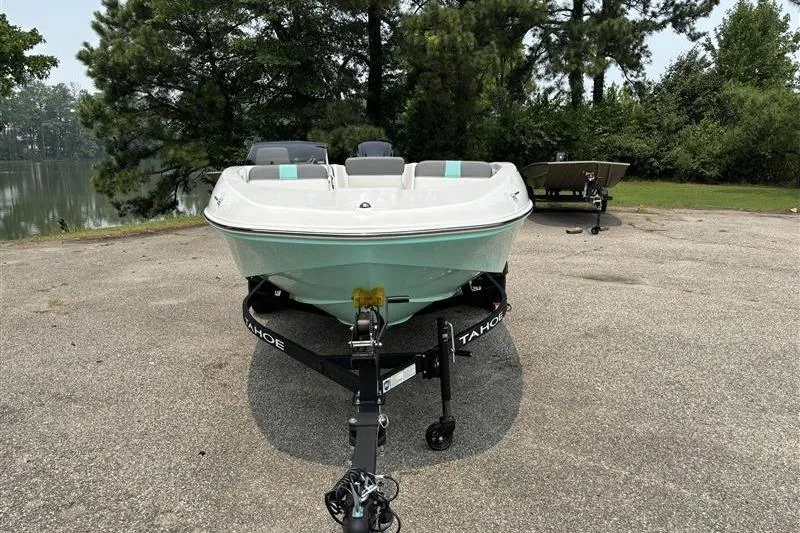 Slide: The Image of 2026 Tahoe T16 boat on trailer, parked near a lake with trees in the background. - 2
