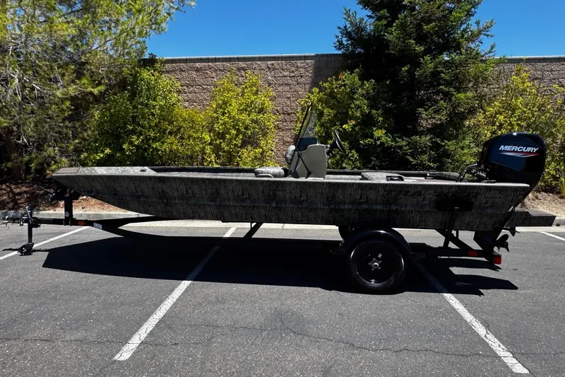 The Image of 2026 Tracker Grizzly 1860 CC boat on trailer, parked outdoors, with Mercury outboard motor. - 0
