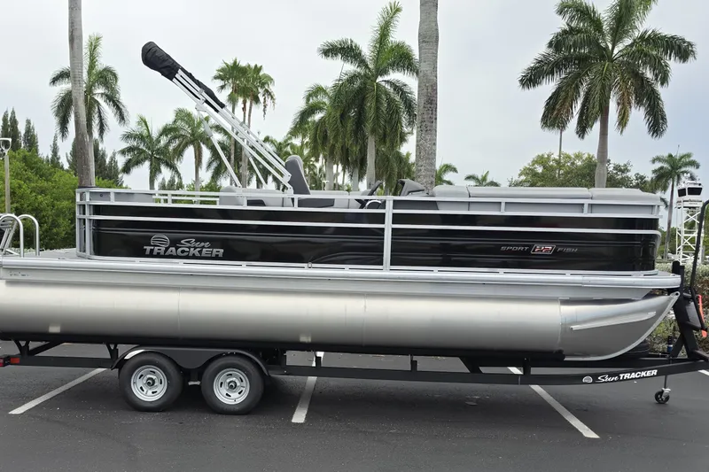 Slide: The Image of 2026 Sun Tracker SportFish 22 XP3 pontoon boat on trailer, surrounded by palm trees. - 1