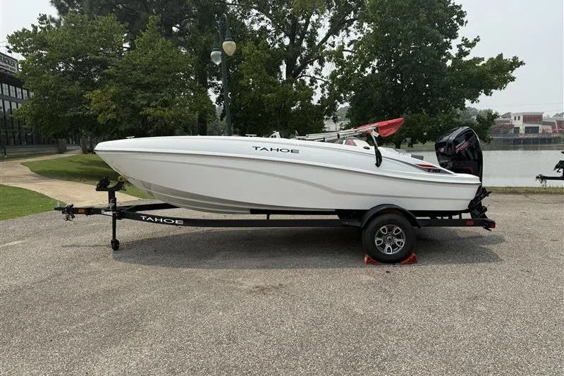 The Image of 2026 Tahoe T18 boat on trailer, parked near a lake with trees in the background. - 0