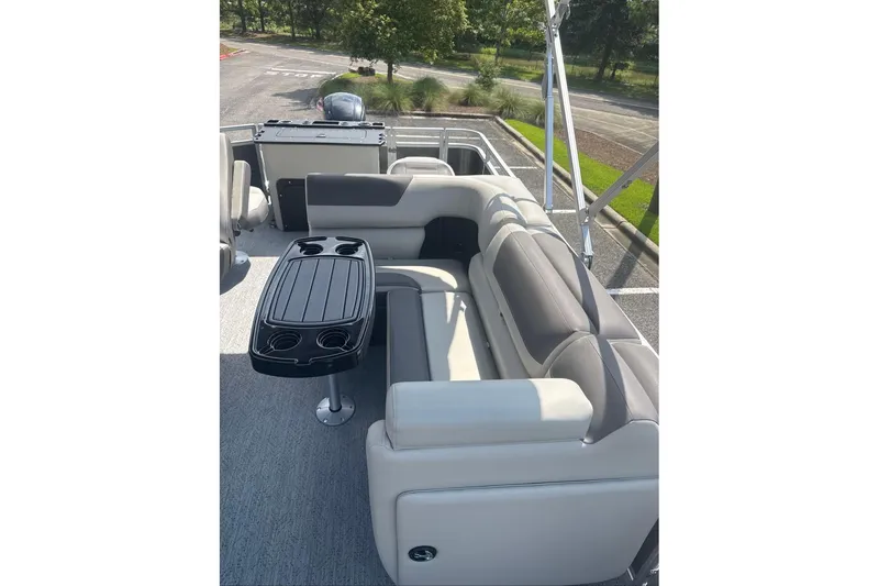 Slide: The Image of 2026 Sun Tracker Fishin' Barge 20 DLX interior with seating and table, parked outdoors. - 6