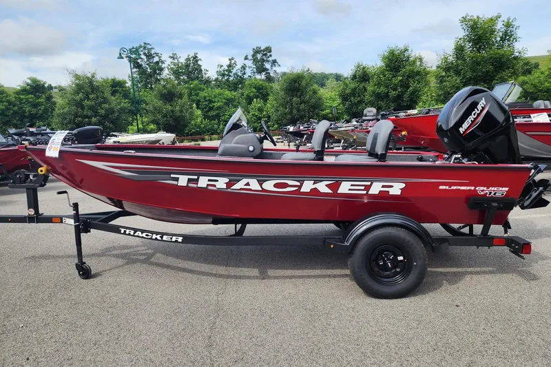 The Image of 2026 Tracker Super Guide V-16 SC boat on trailer, red with Mercury engine, parked outdoors. - 0