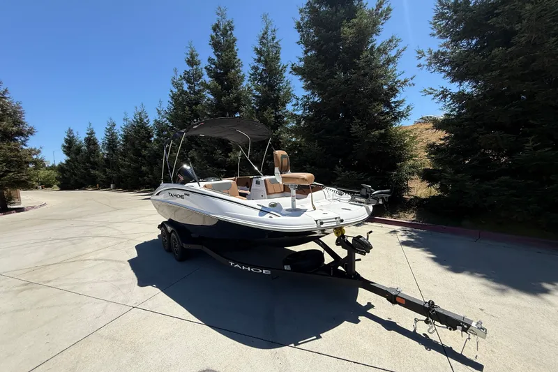 Slide: The Image of 2026 Tahoe 1950 boat on trailer, parked outdoors with trees in background. - 2