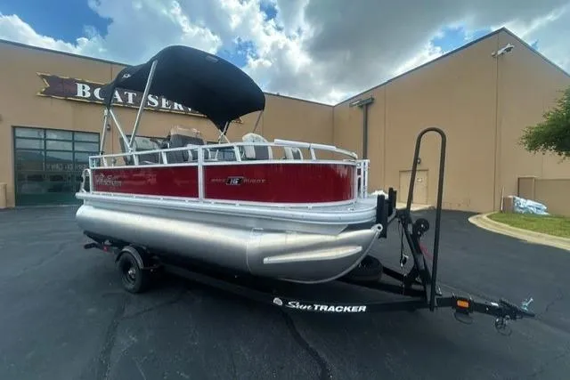 The Image of 2026 Sun Tracker Bass Buggy 16 XL Select pontoon boat on trailer, parked outside a boat service center. - 0