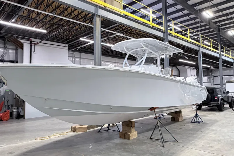 Slide: The Image of 2026 Jupiter 32 boat in a warehouse, elevated on stands, showcasing sleek design. - 19