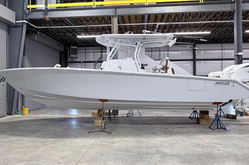 Slide: The Image of 2026 Jupiter 32 boat in a warehouse, elevated on stands, showcasing sleek design. - 21