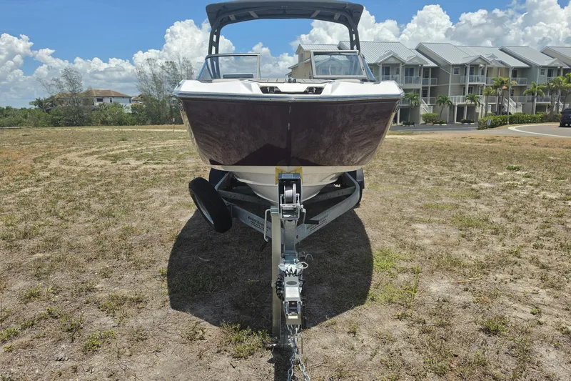 Slide: The Image of 2022 Yamaha Boats 252SD on trailer, parked on grassy area with houses in background. - 10