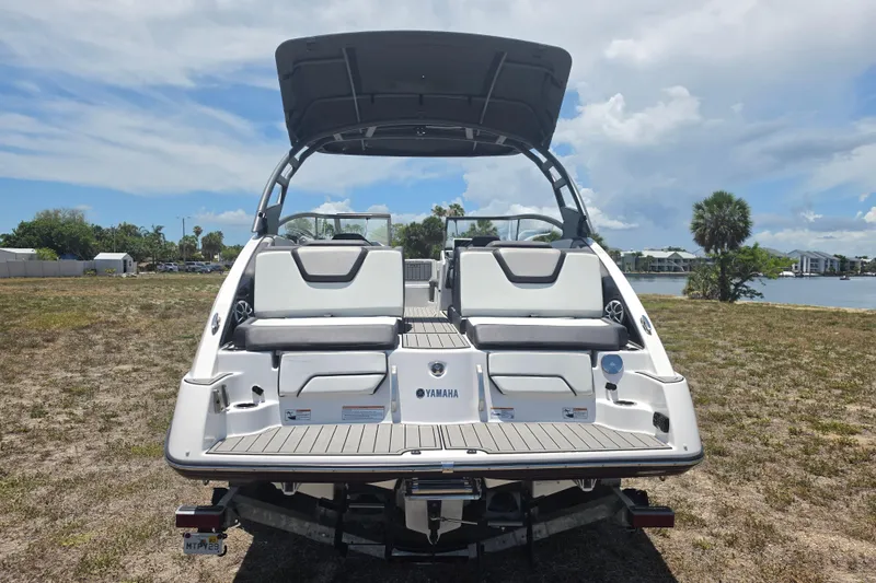 Slide: The Image of 2022 Yamaha Boats 252SD on trailer, rear view, with open canopy, near water and grassy area. - 4