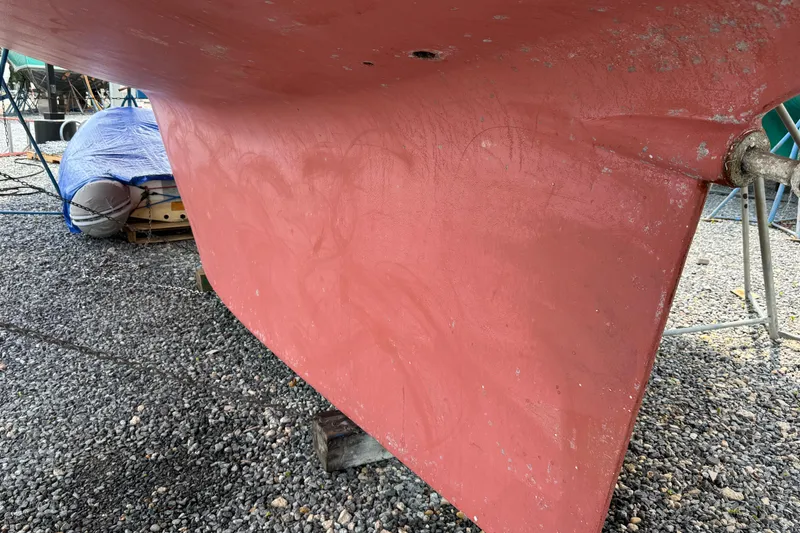 Slide: The Image of Red keel of a 2007 Hylas H49 sailboat on gravel, with covered items nearby. - 56