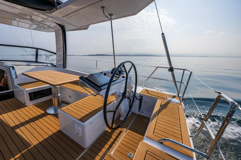 Slide: The Image of 2025 Hanse 460 yacht cockpit with wooden deck, steering wheel, and seating area on calm sea. - 5