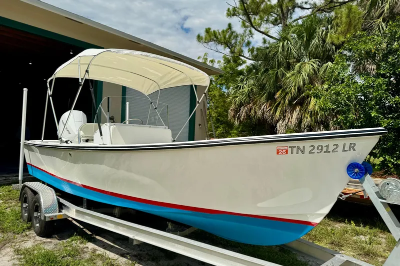 Slide: The Image of 2025 Rambo 22 Center Console boat on trailer, white with blue and red accents, parked outdoors. - 11