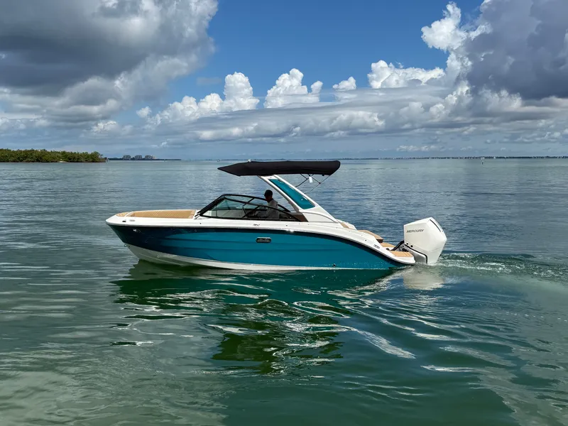 Slide: The Image of A 2026 Sea Ray SDX 230 Outboard cruising on calm waters. It features a blue and white design with a black canopy. - 0