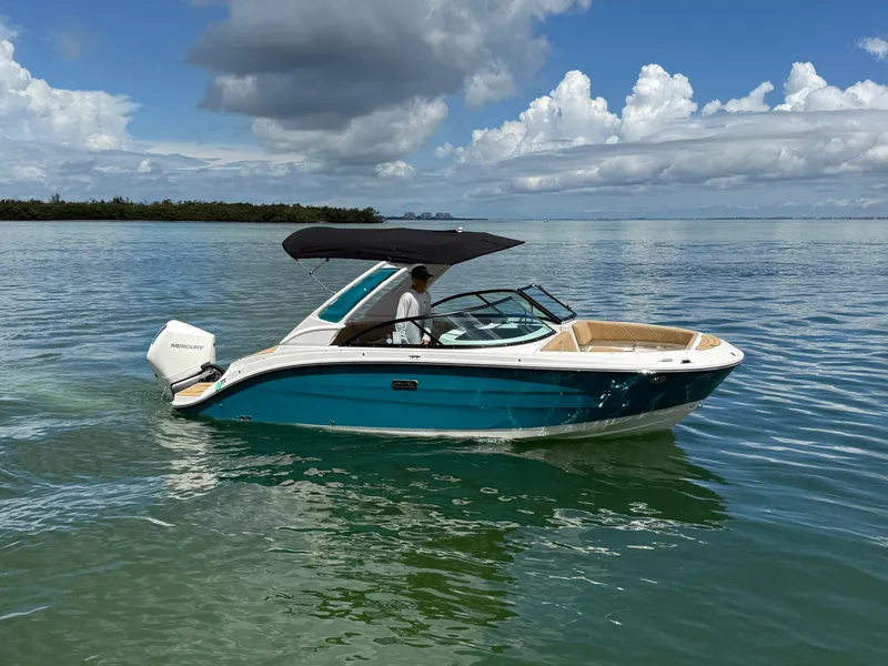 Slide: The Image of A 2026 Sea Ray SDX 230 Outboard cruising on calm waters. It features a blue and white design with a black sunshade. - 3