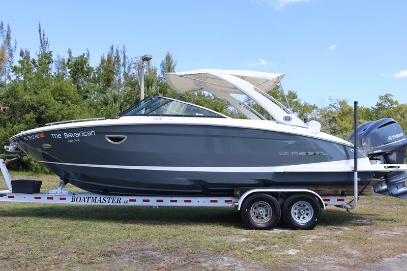 Slide: The Image of 2019 Regal 29 OBX boat on trailer, side view, outdoors with trees in background. - 2