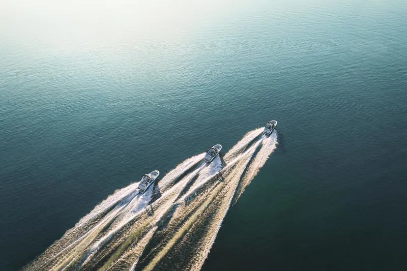 Slide: The Image of Three boats travel in formation across calm water, leaving long wakes and reflecting sunlight. - 19