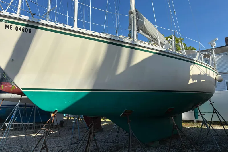 Slide: The Image of 1994 Caliber Cutter Rig sailboat on stands, white hull with green stripe, sunny day. - 10