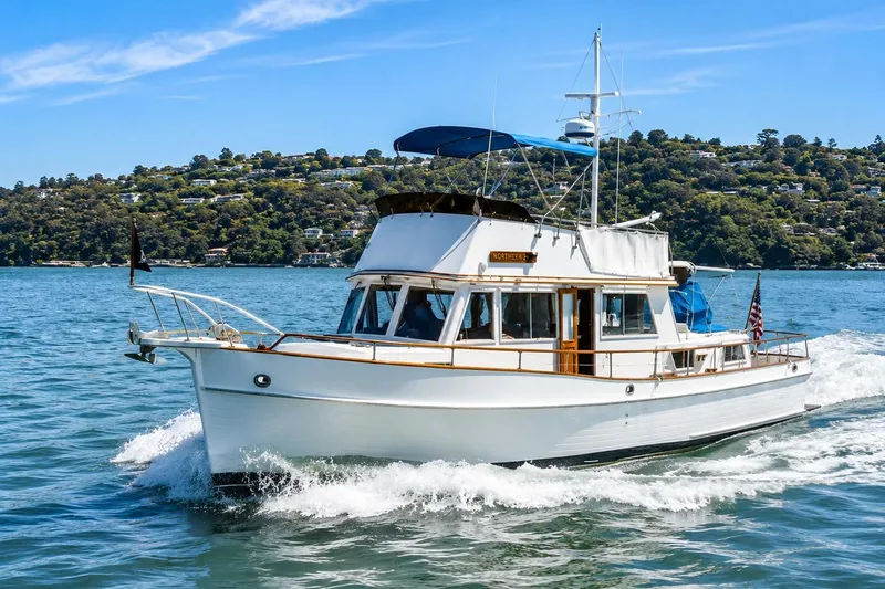 The Image of 1989 Grand Banks 42 Classic yacht cruising on a sunny day, scenic hillside backdrop. - 0