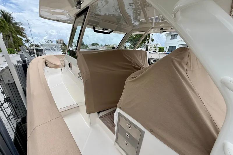 Slide: The Image of 2018 Pursuit S 408 Sport boat interior with covered seating and helm, docked near palm trees. - 13