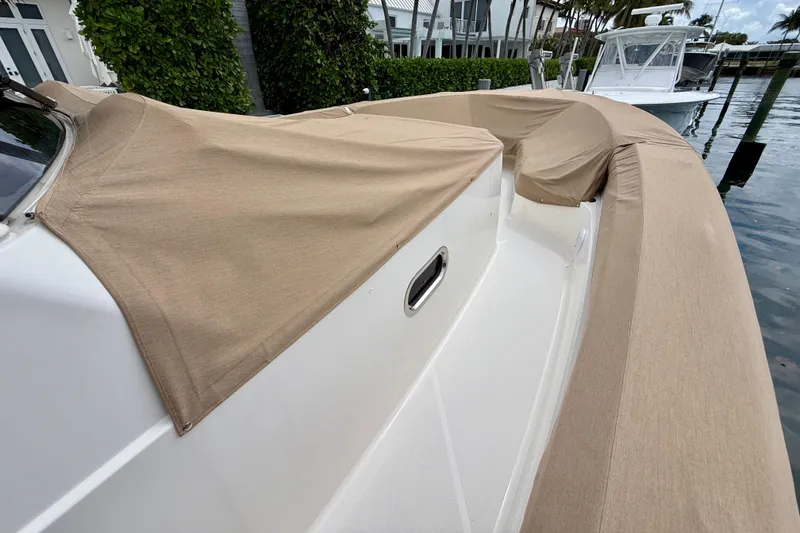 Slide: The Image of 2018 Pursuit S 408 Sport boat with tan covers docked by waterfront homes. - 18