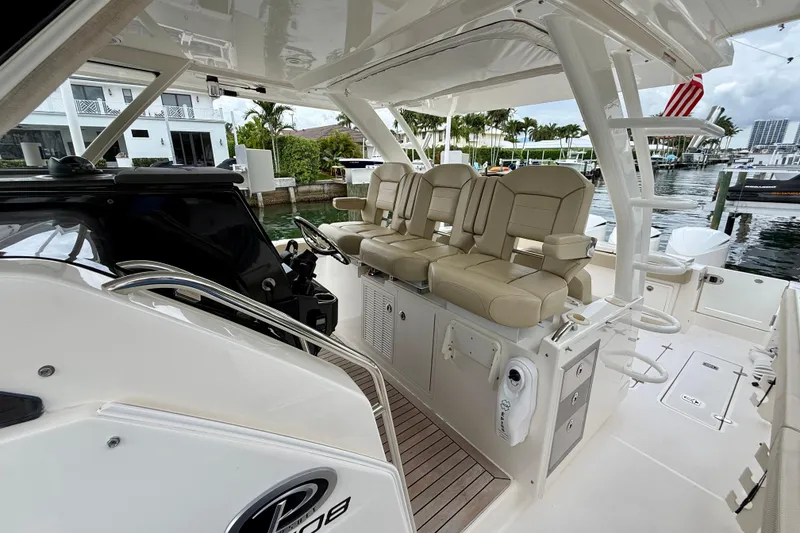 Slide: The Image of 2018 Pursuit S 408 Sport boat interior with beige seating and helm, docked by waterfront homes. - 54