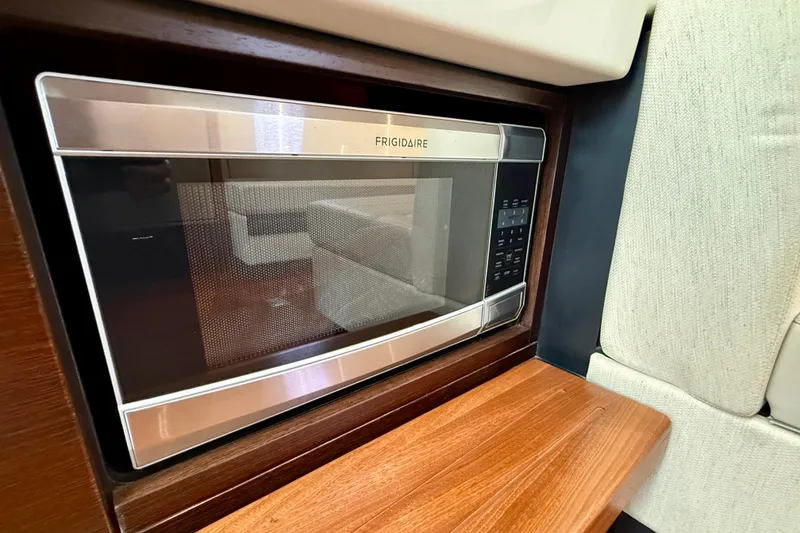 Slide: The Image of Frigidaire microwave in 2018 Pursuit S 408 Sport boat interior, featuring wood and fabric accents. - 83