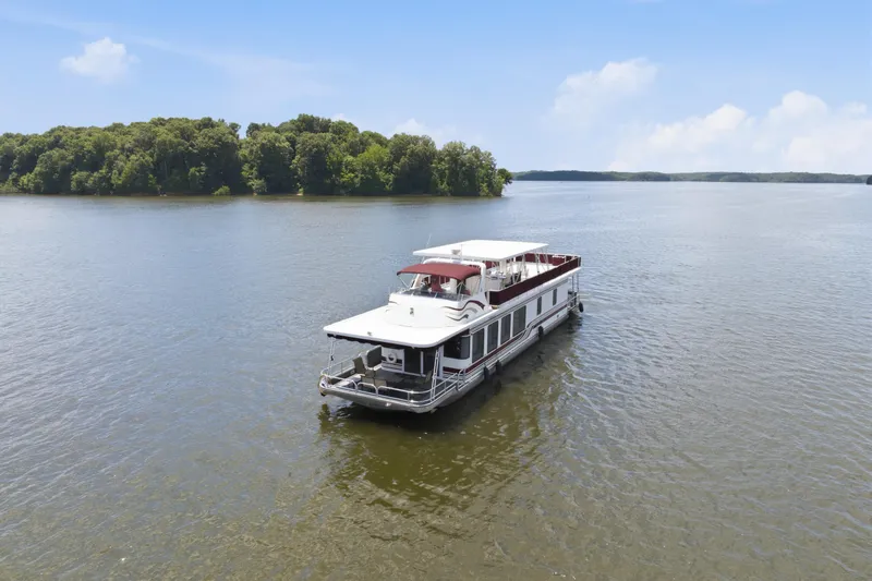 Slide: The Image of 2002 Sumerset 16x75 houseboat cruising on a serene lake with lush green shoreline. - 12