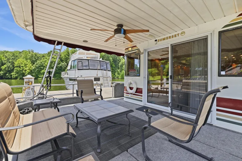 Slide: The Image of Outdoor seating area on a 2002 Sumerset 16x75 houseboat, featuring a ceiling fan and scenic lake view. - 23