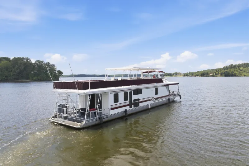 Slide: The Image of 2002 Sumerset 16x75 houseboat cruising on a serene lake under a clear blue sky. - 4