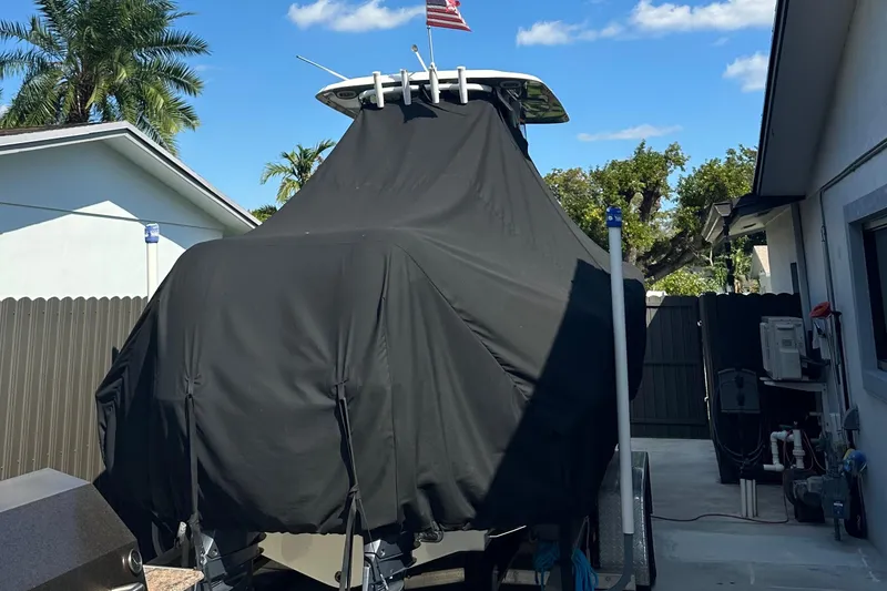 Slide: The Image of 2019 Sea Hunt Gamefish 25 boat covered, parked in driveway with palm trees and blue sky. - 16