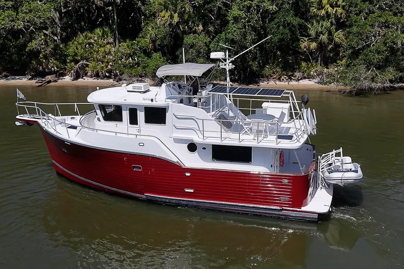 Slide: The Image of 2003 Magna Marine Nova Scotia 47 boat with red hull cruising near lush shoreline. - 1