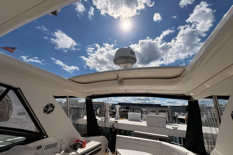 Slide: The Image of 2019 Sea Ray Sundancer 320 interior with open sunroof, sunny sky, and marina view. - 15