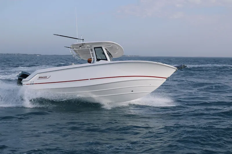 Slide: The Image of A 2027 Boston Whaler 250 Outrage speeds across the water, with a clear sky in the background. - 2