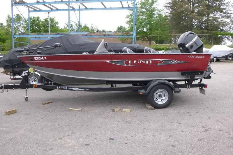 Slide: The Image of 2012 Lund 1775 Impact fishing boat on trailer, red and silver, parked outdoors. - 1
